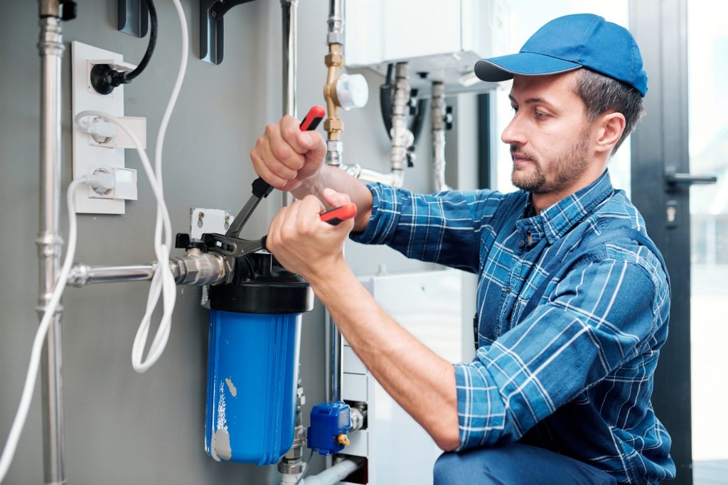 young plumber or technician installing or repairing system of water filtration